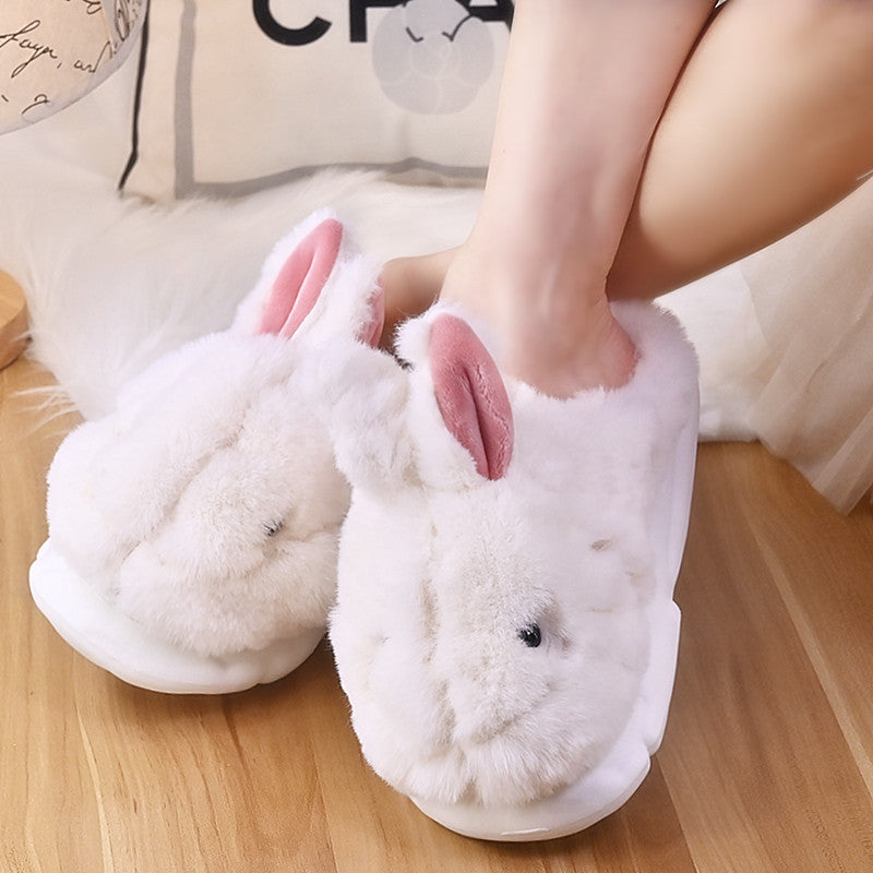White Rabbit slippers with pink ears worn by a person on a wooden floor.