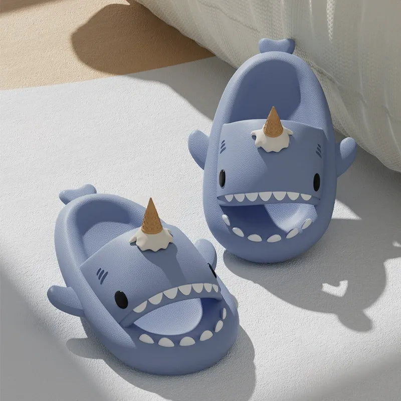 Two blue shark-shaped slippers with a unicorn horn on a light surface.