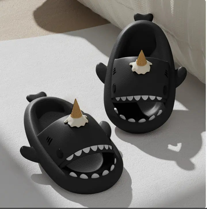 Black shark-shaped slippers with unicorn horns on a light surface