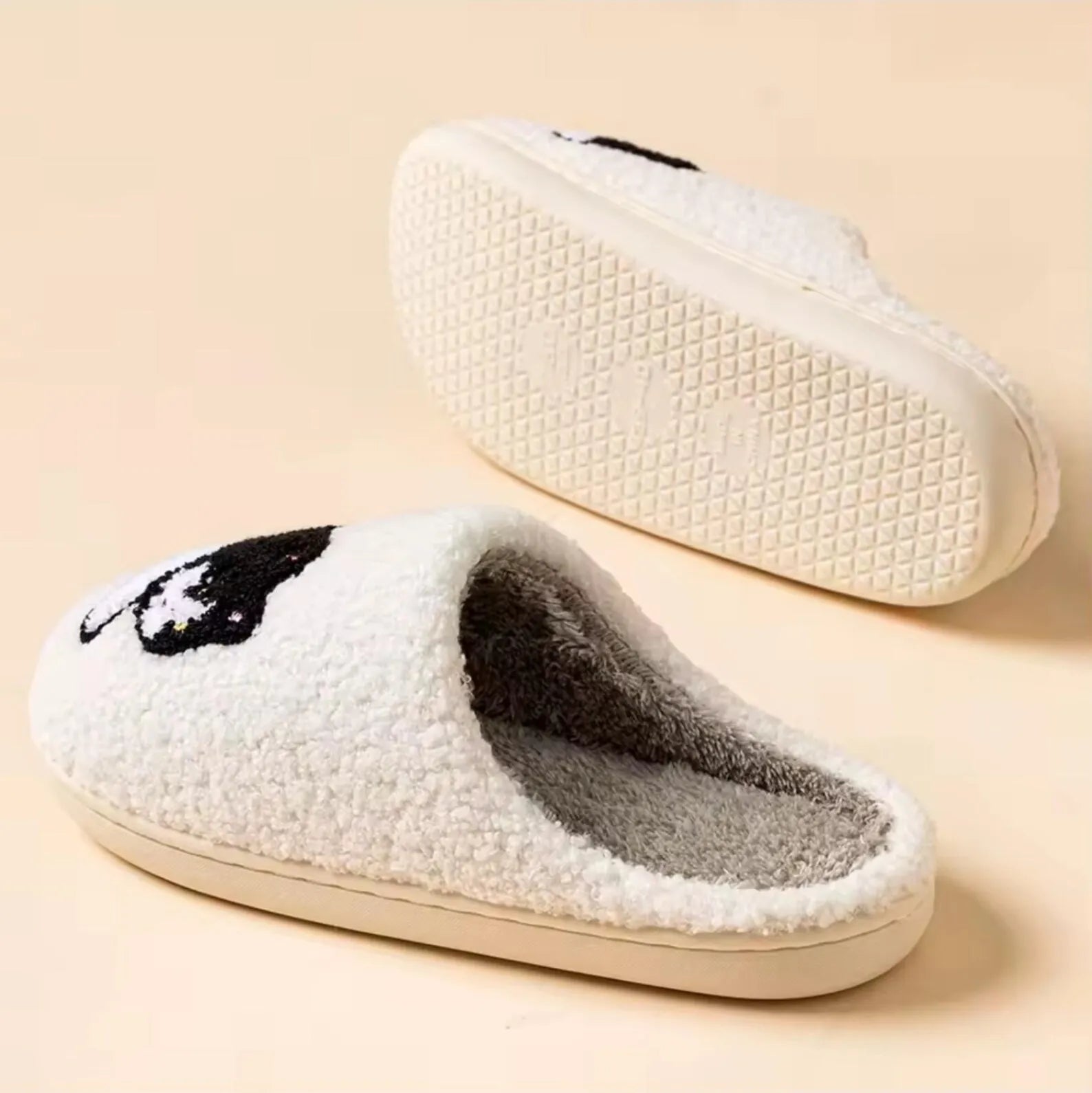 White slippers with black paw print design on a beige background