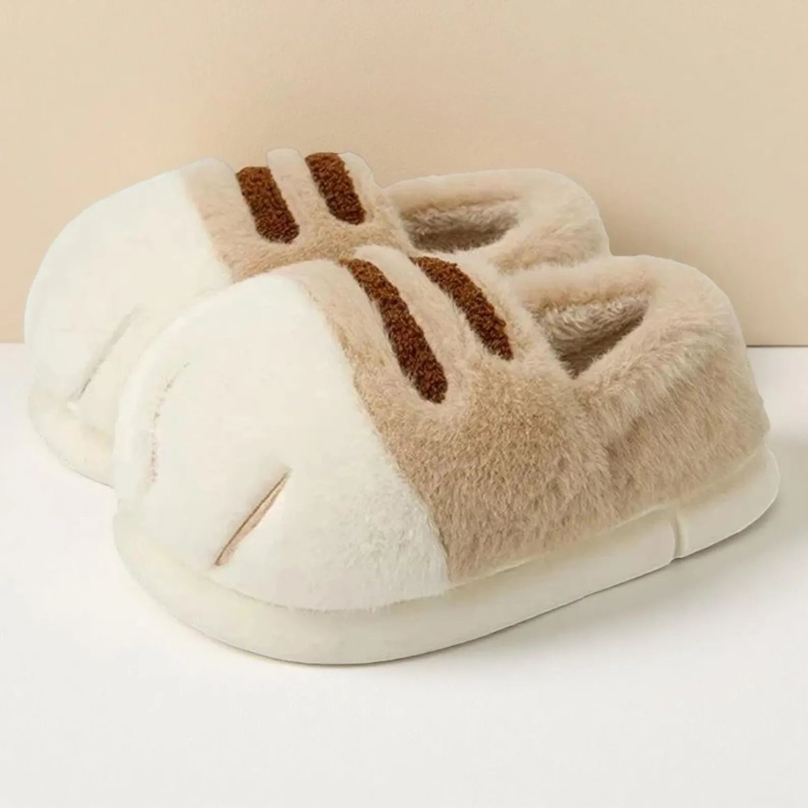 Pair of plush slippers with brown accents on a white surface.