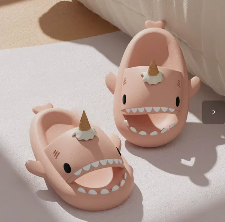 Pink shark-shaped slippers with unicorn horns on a light surface