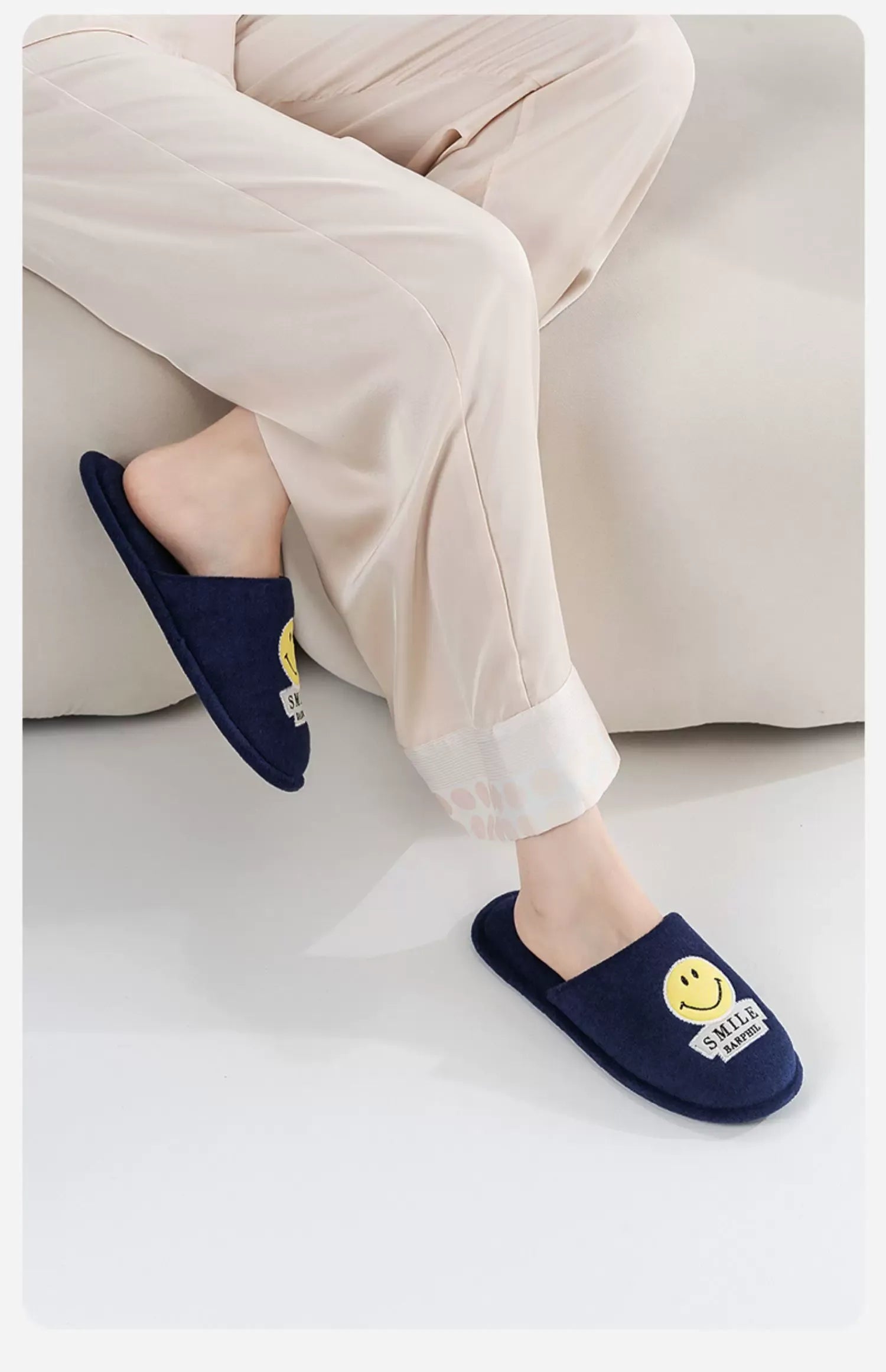 Navy blue slippers with smiley face design worn by a person on a light-colored floor.